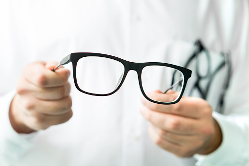 istockphoto-873462548-170667a Optician holding glasses. Eye doctor showing new lenses. Professional optometrist in white coat.
